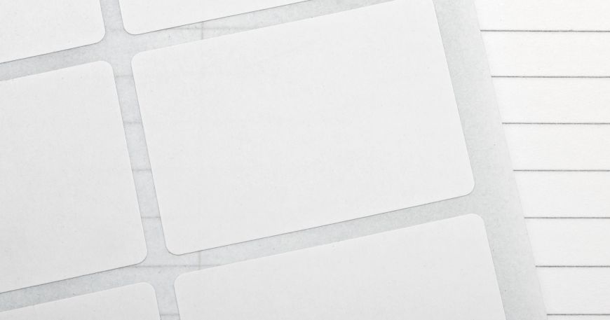 A sheet of labels resting on top of a note pad; the face material is the matt white paper layer of each label. 