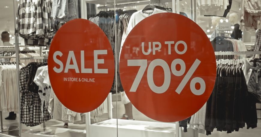 Two window stickers in a clothing store advertising a sale; a temporary label is often used for short term applications (like labels promoting a sale) and delicate materials (like glass windows).