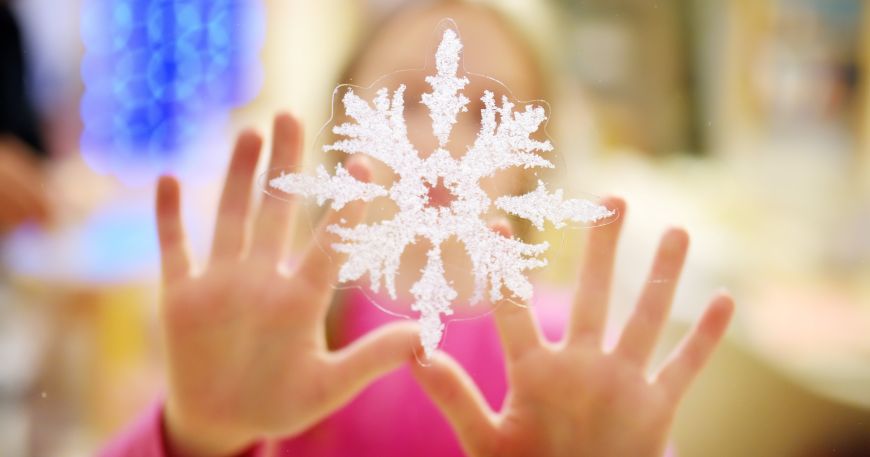 A child sticks a transparent label with a snowflake design onto a window. 