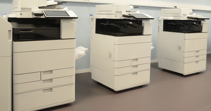 A row of three photocopiers in an office room.