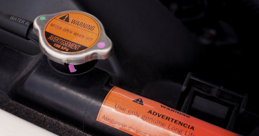 Two warning labels stuck onto parts of a car's engine. High temperature adhesives are designed to withstand exposure to hot temperatures. 