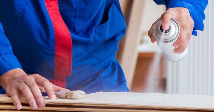 A worker sprays a clear coat onto the surface of a material.