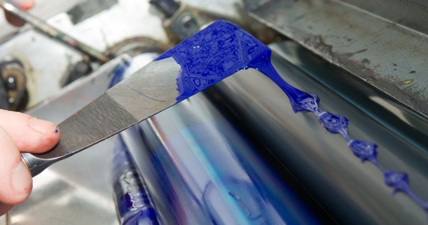 Cyan ink being applied with a filling knife to the die cutter of a commercial printing press.