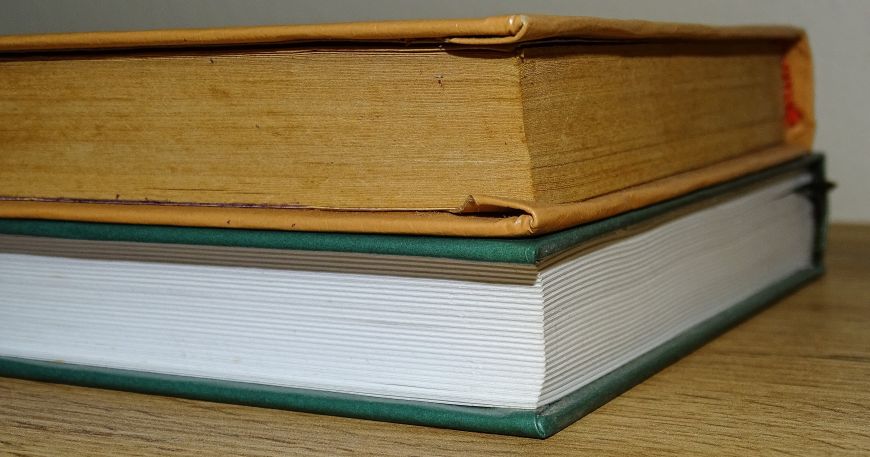 Two books are stacked in a pile; the older top book shows discolouration of its pages compared to the newer bottom book.