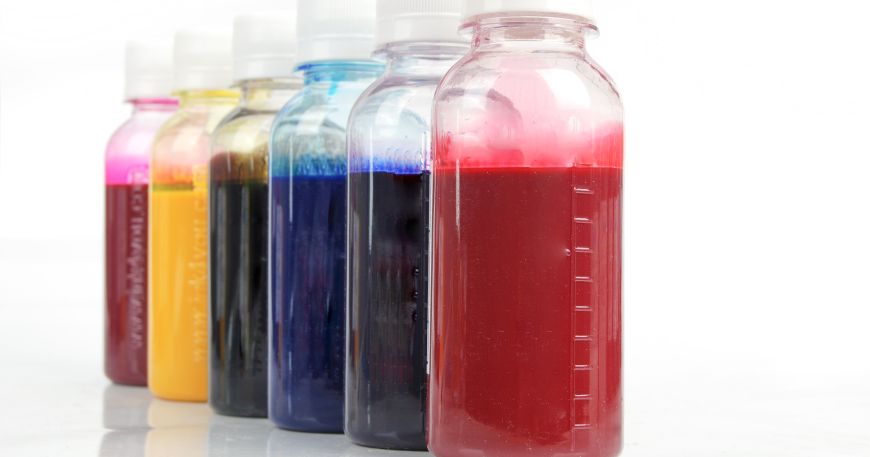 Six bottles containing liquid inks in different colours; the inks are red, blue, cyan, black, yellow, and magenta in colour. 