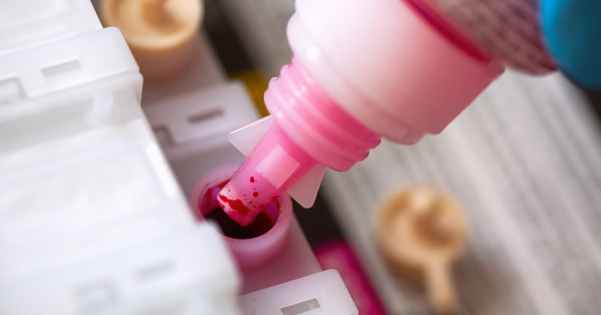 A person uses a bottle of magenta ink to refill a cartridge in an inkjet printer.