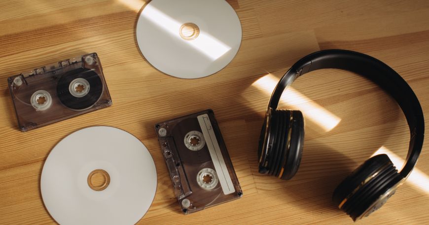 Two CDs and two audio cassette tapes lie on a wooden table next to a pair of headphones. We supply media labels for CDs, DVDs, audio cassette tapes, videos, and digital media storage devices.