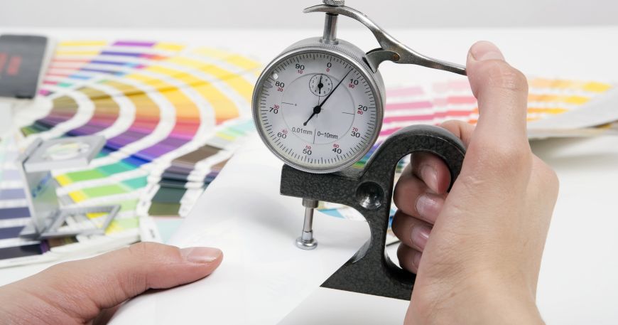A person uses a micrometer to measure the thickness of a sheet of paper; mil is one unit of measurement used for sheets of materials.