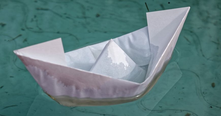 A paper boat floating on water; the paper has begun to absorb water, which is increasing its moisture content.