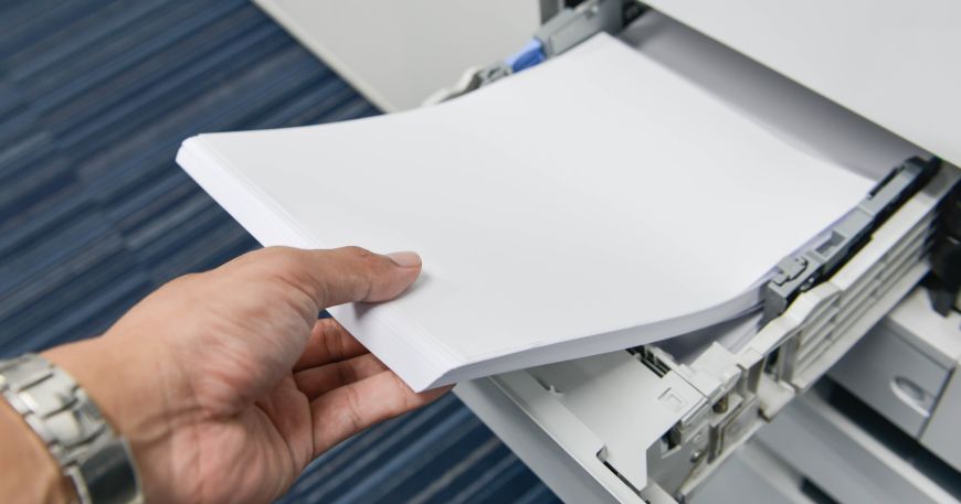 A person feeds a stack of paper into a printer narrow edge leading.