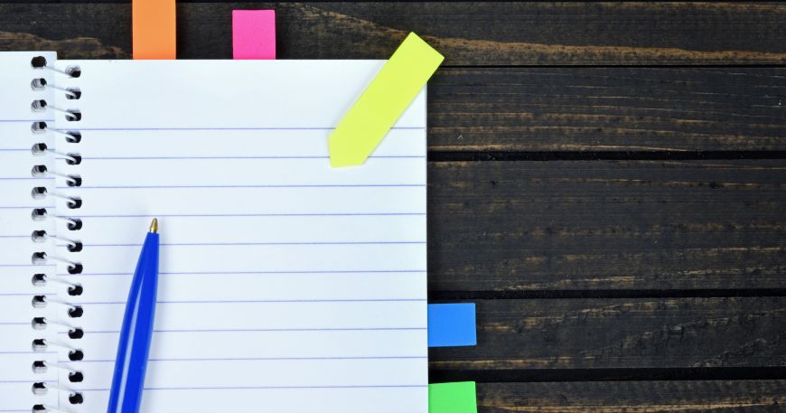 A notebook with a set of sticky tabs or page markers; four tabs have been stuck onto individual pages. Sticky page markers use peelable adhesives because they don't damage the pages of the notebook when the tabs are removed.