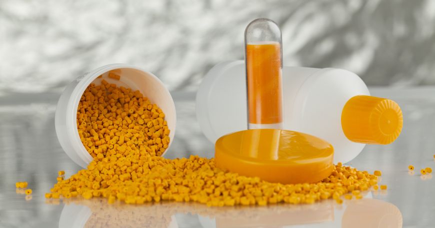 A tub of orange granules of a polymer sits next to three containers, which have been entirely or partially made out of an orange polymer.