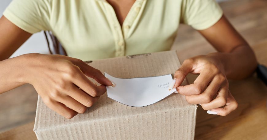 A persona applies a pressure senstive label onto a cardboard box.