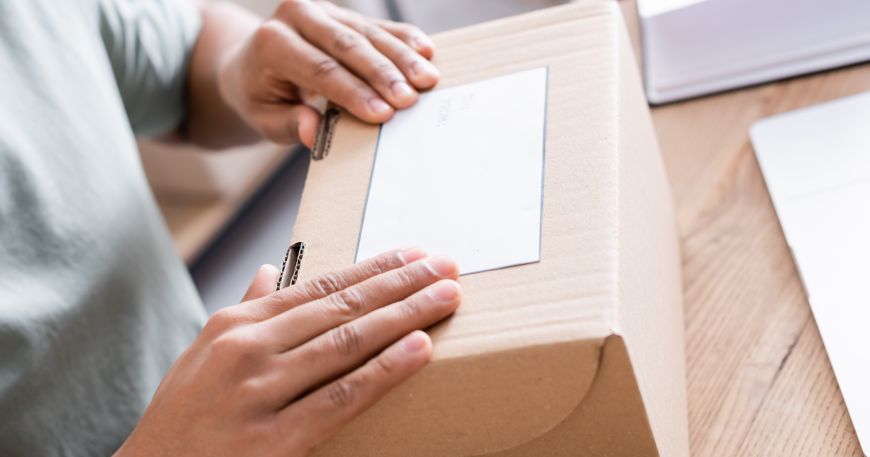 A person applies a pressure sensitive laminated onto a cardboard box.