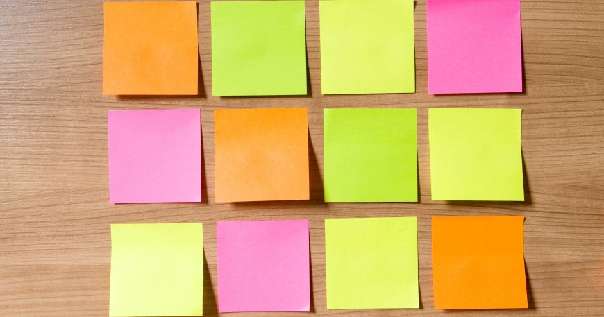 A number of post it notes on a wodden desk; a removable label can be stuck onto one item or surface and then removed without damaging that item or surface.