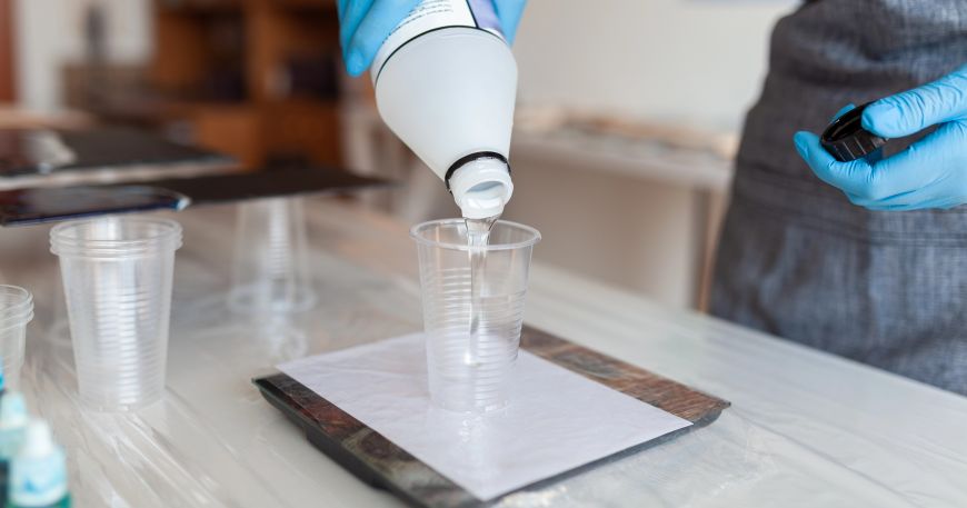 A resin is poured from a container into a plastic cup.