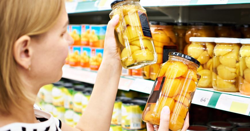 A person choosing products in a supermarket. Each jar has a primary label (right jar) and a secondary label (left jar). A secondary label provides more detailed product information and is usually positioned on the back, side, or bottom of a product.