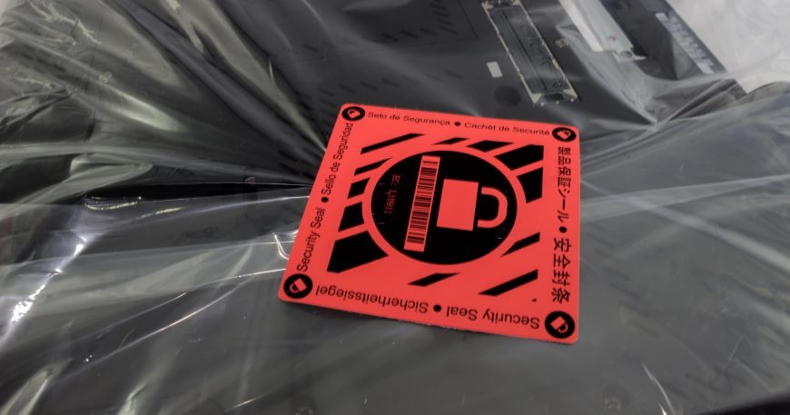 A red security label that has been applied onto packaging that contains a laptop.