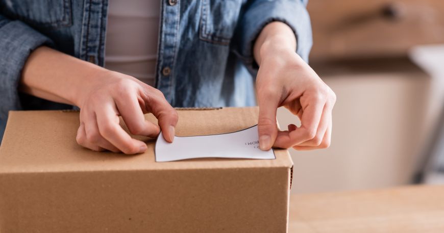 A person applies a self adhesive label onto a cardboard box.