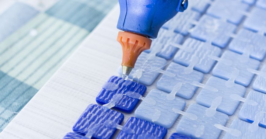 A person gluing together mosaic tiles; the glue currently being applied is in a liquid state, while the glue that has been applied earlier has set into a solid state. 