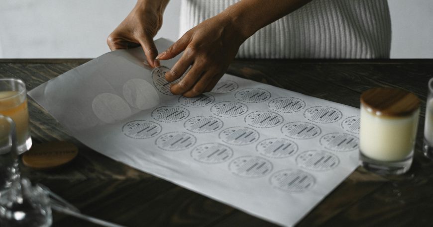 A person removes a label from a sheet of labels; sheet labels are supplied on a flat backing sheet. 