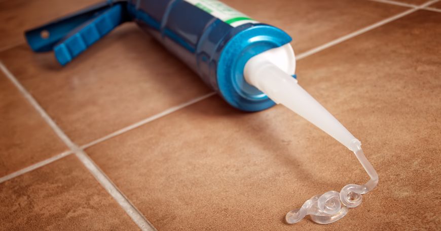 A silicone gun lying on a tiled floor. 