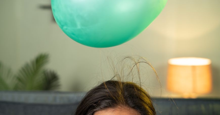 A demonstration of static cling; a balloon is used to generate static and attract a person's hair so it sticks to the balloon.