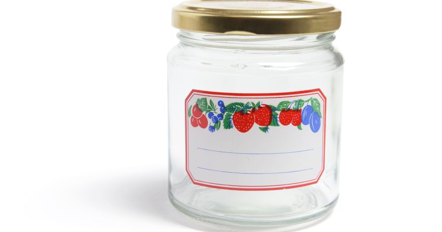 A glass jar that has been labelled with a label that has been printed with a design showing fruit and space to add the contents. Both the glass surface of the jar and the face material of the label can be called 