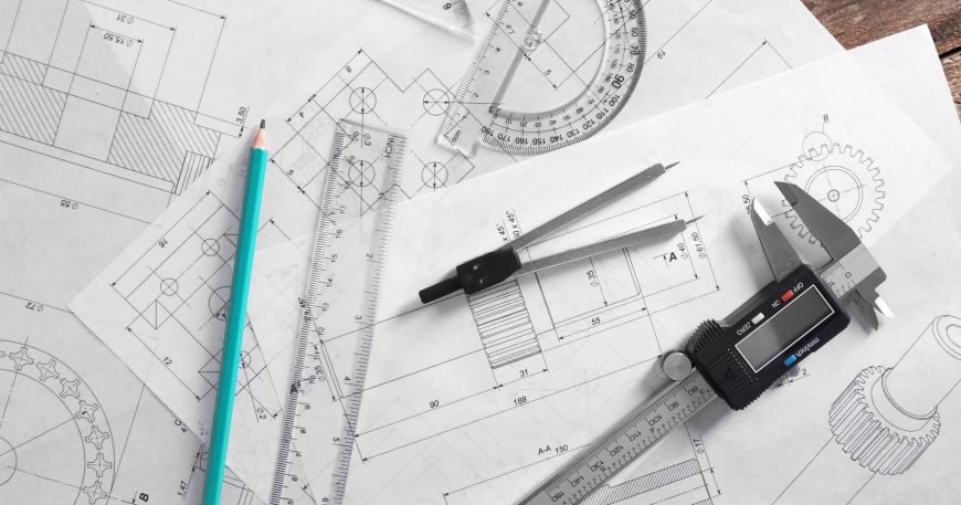 A set of measuring tools sit on top of engineering drawings of various parts; all manufactured products are made to a tolerance, which is an allowable deviation from the given specifications under quality guidelines.