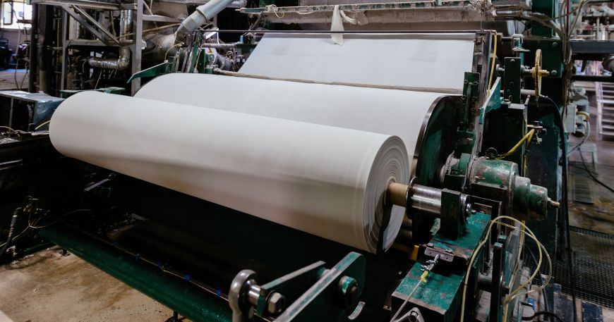 A roll of uncoated paper being processed during manufacturing; as part of the manufacturing process, the paper will have coatings applied and will be cut to the required size.
