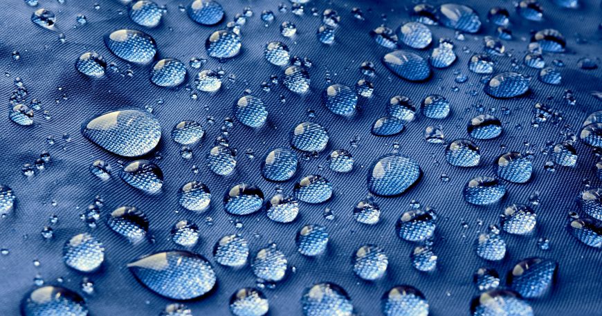 Drops of water on a blue waterproof fabric; the waterproof material does not allow the water to penetrate into the material so the droplets sit on the surface. 
