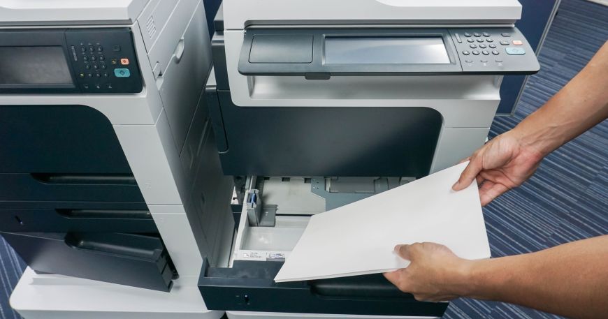 A person feeds a stack of paper into a printer wide edge leading.