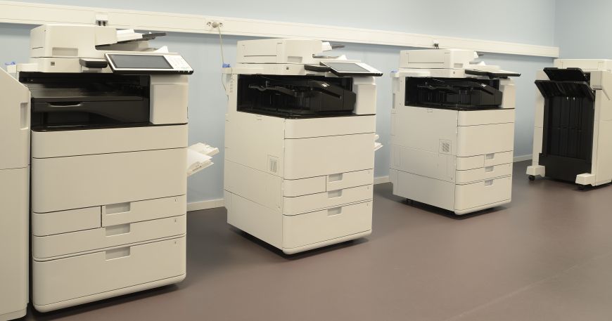Four photocopier machines are lined up in an office room; photocopiers use xerography to produce printed copies of documents.