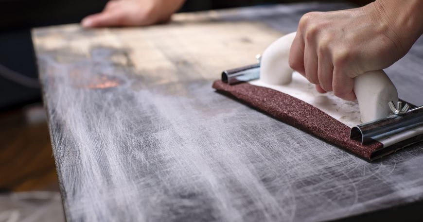 A wooden table is sanded down using sandpaper. Sandpaper is a highly abrasive material, while woods have different levels of abrasion resistance.