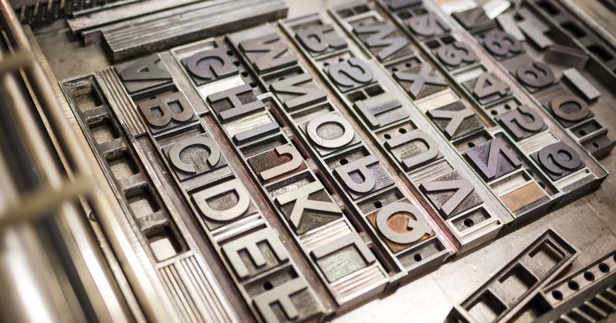 A flat image carrier on a letterpress printer is filled with the individual raised metal types for the letters A to Z and the numbers 0 to 9.