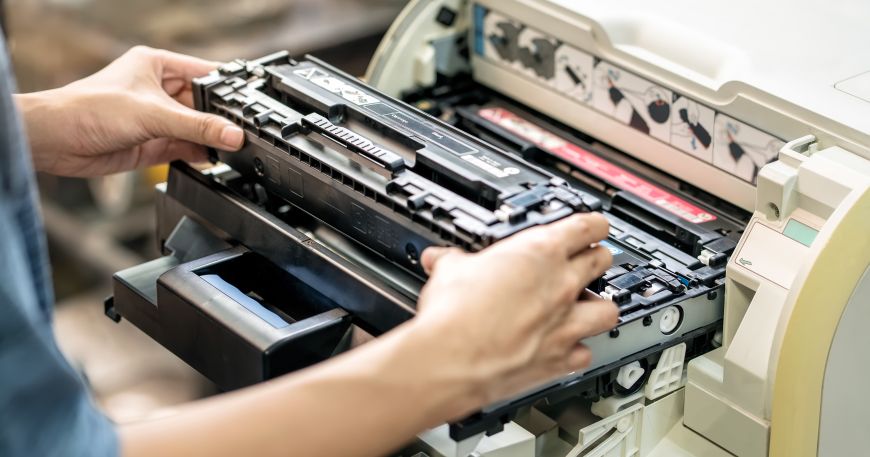 A person replaces a toner cartridge in a laser printer.