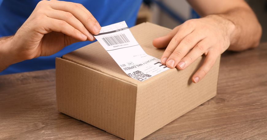 A person applies a self adhesive label to a cardboard parcel.