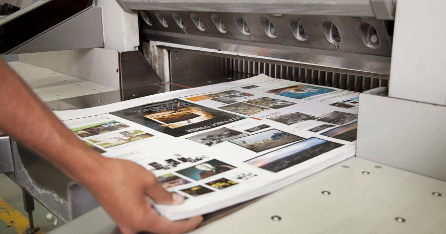A person removes a stack of printed sheets from a printing press; materials that are used to make printed media must have good printability in order to produce good print quality and accuracy.