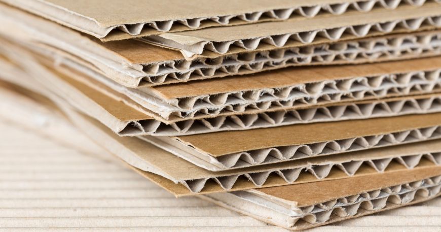A close up of corrugated cardboard sheets made up of three to five layers. Each sheet has a flat ply for the top and bottom layers with wavy ply in between (the five layered sheets have an additional flat ply between two wavy ply).