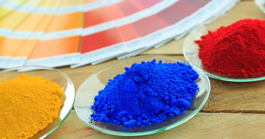 Three different colours of pigment are sat in glass dishes next to a colour chart. 