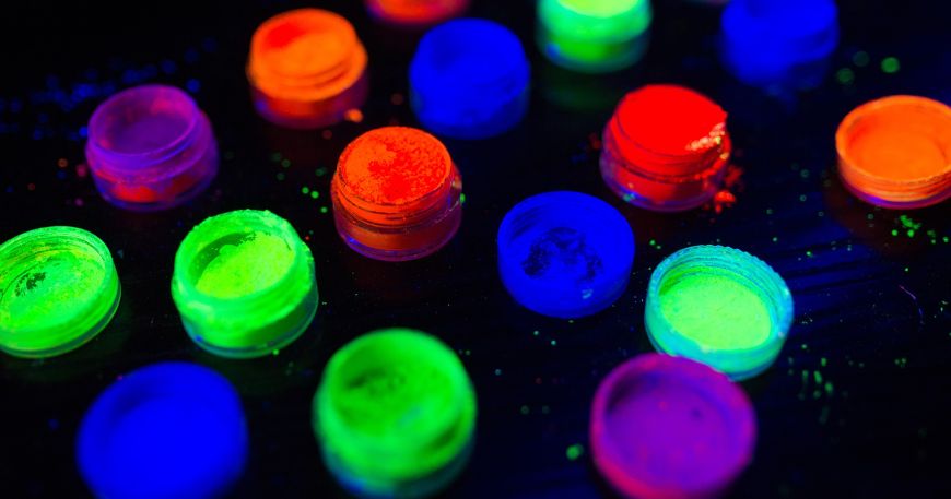 Small tubs of phosphorescent powders of different colours on a black table.