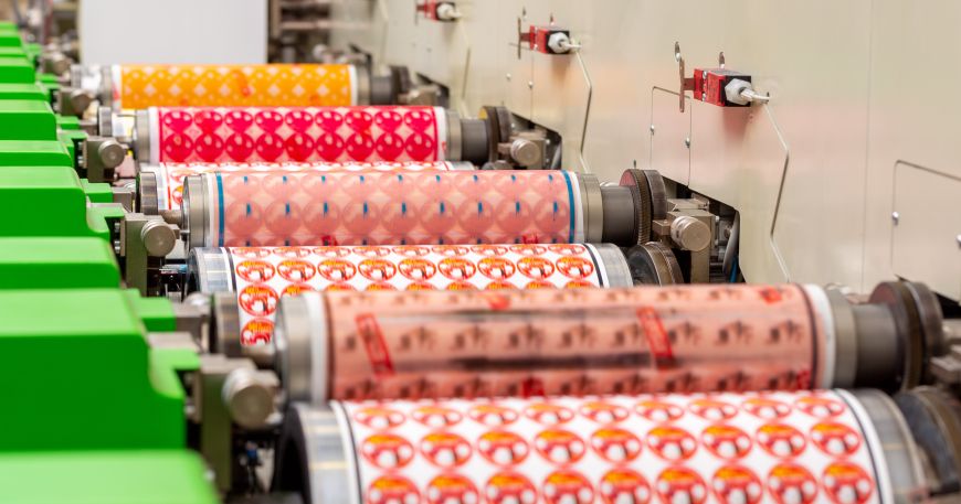 A close up of the yellow, magenta, cyan and black print cylinders in a flexographic printer. Each cylinder carries a photopolymer relief plate.