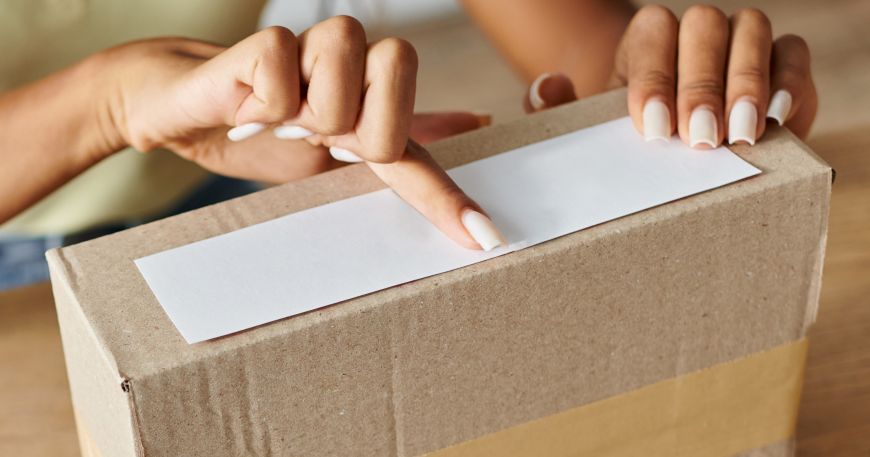A woman applies pressure to a self adhesive label, which she is sticking onto a cardboard box.