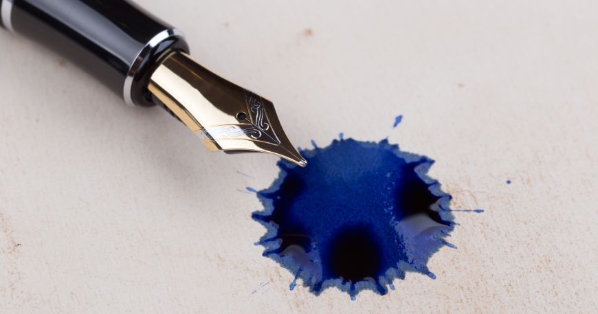 A blot of ink from a fountain pen on a wooden desk; the permeability of wood means that some of the ink has passed into the wood but some remains on the surface.