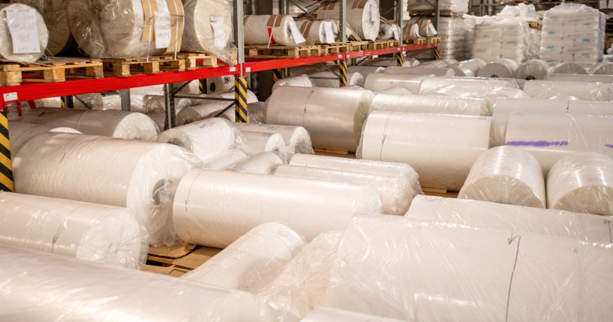 Rolls of white polyethylene film wrapped in clear plastic bags in a warehouse.