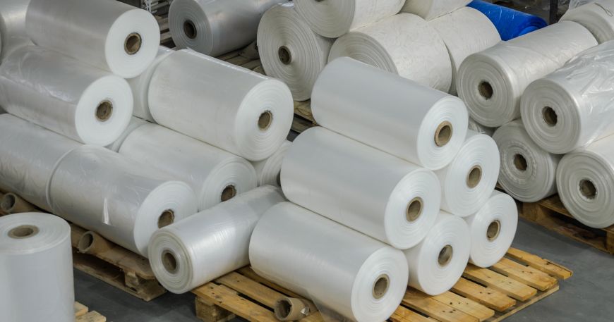 Stacks of rolls of white polyester film on pallets in a warehouse.