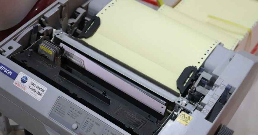A dot matrix printer loaded with pin feed paper; pin feed labels have holes in the left and right margin to guide the continuous sheet (or web) through the printer.