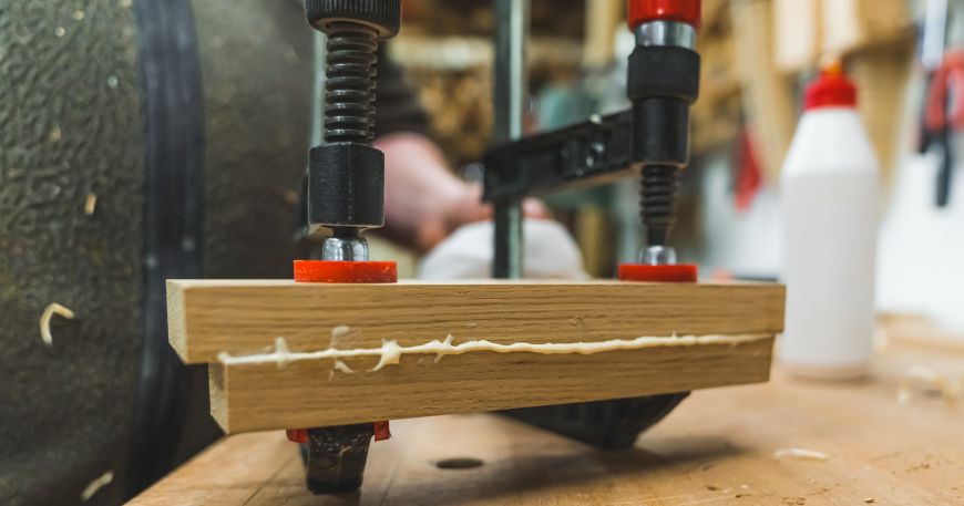Adhesive bleed in two blocks of wood; the adhesive that has been applied between the two blocks has moved out of place due to the pressure applied by the clamps holding the wood in place.