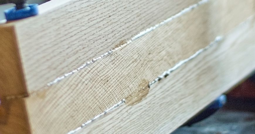 An adhesive that has begun to creep out of the gaps between three blocks of wood that are being glued together.