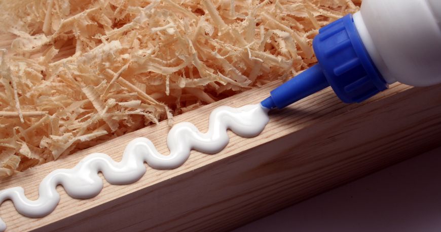 An adhesive being applied out of a bottle onto a block of wood.